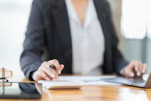 Shot of a young professional woman sitting at desk in front of laptop and using mobile phone working on business contract.