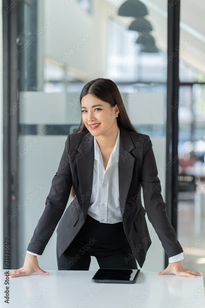 Portrait of beautiful young woman standing in front of glass board and smiling on camera. Female office worker using laptop in company. Portrait of beautiful young woman standing in front of glass board and smiling on camera. Female office worker using laptop in company.