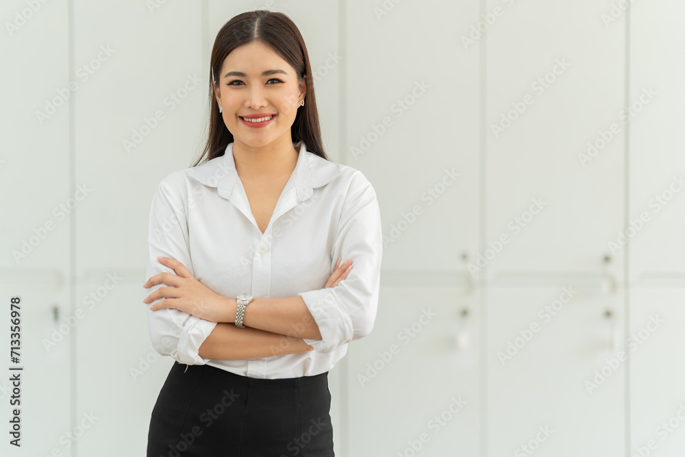 Portrait of beautiful young woman standing in front of glass board and smiling on camera. Female office worker using laptop in company.