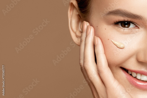 Foundation make up.  Skincare model. Close up portrait of beautiful young woman with perfect skin and bb cream smear isolated on beige background. Beauty treatment and spa concept. photo