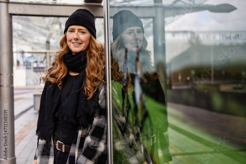 Woman in her mid-thirties with long red hair wearing a cap and black clothing in an urban location. photo