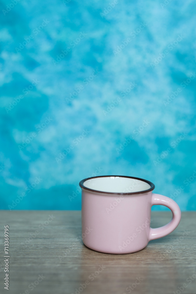 Pink coffee cup on wooden table and blue background. Copy space.