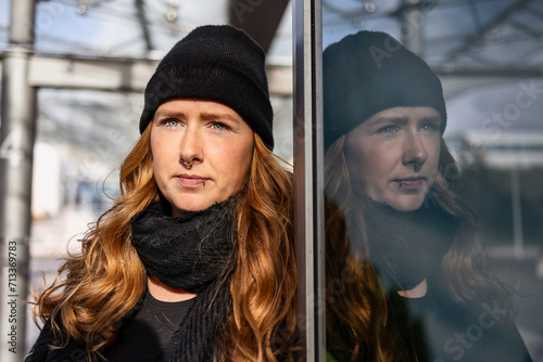 Woman in her mid-thirties with long red hair wearing a cap and black clothing in an urban location. photo