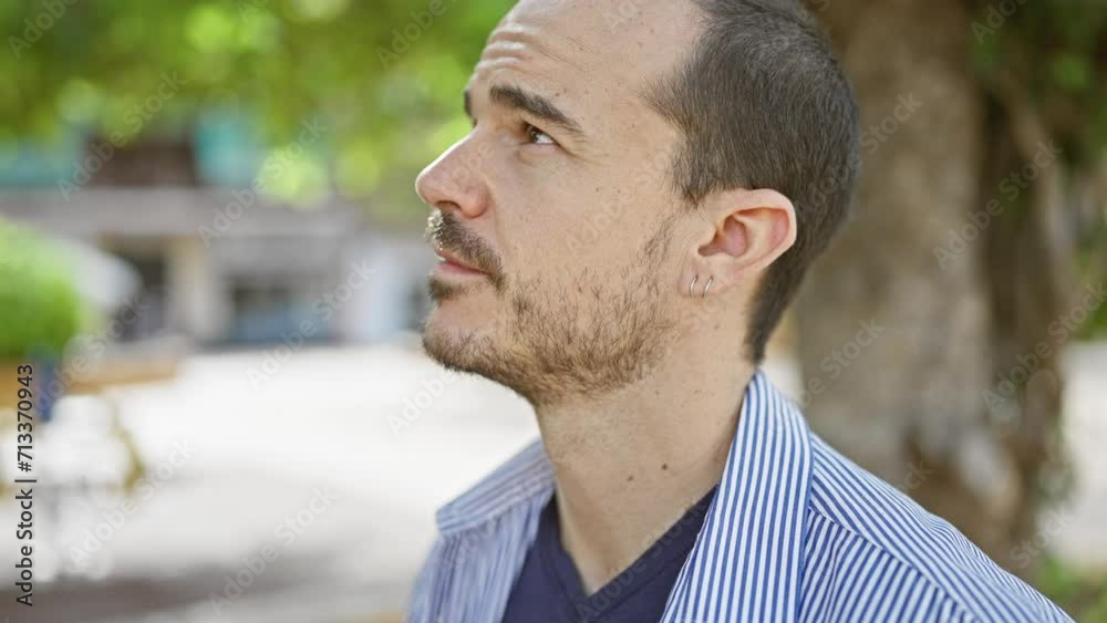 Hispanic man with beard and ear piercing, looking thoughtful on urban street. Hispanic man with beard and ear piercing, looking thoughtful on urban street.