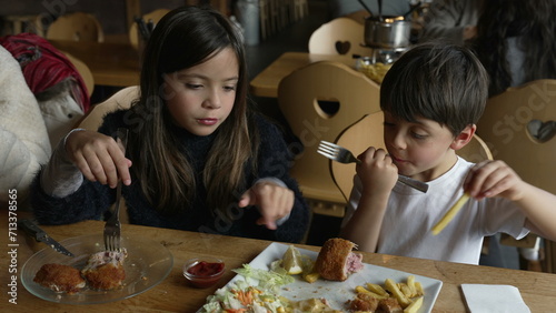 children enjoying mealtime at restaurant - small siblings, brother and sister interaction at diner eating food. Plate of milanese meat with fries