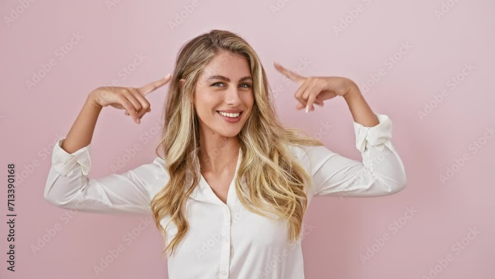 Cheerful, smart blonde woman having an 'aha!' moment, joyfully pointing fingers at head over isolated pink background, embodying pure positive vibes.