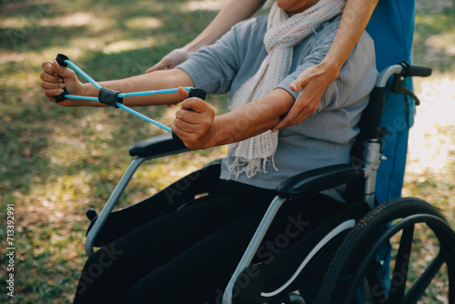 Young nurse or physiotherapist in scrubs helping a happy retired old woman do fitness exercises with light weight dumbbells at home. Concept of physiotherapy for seniors