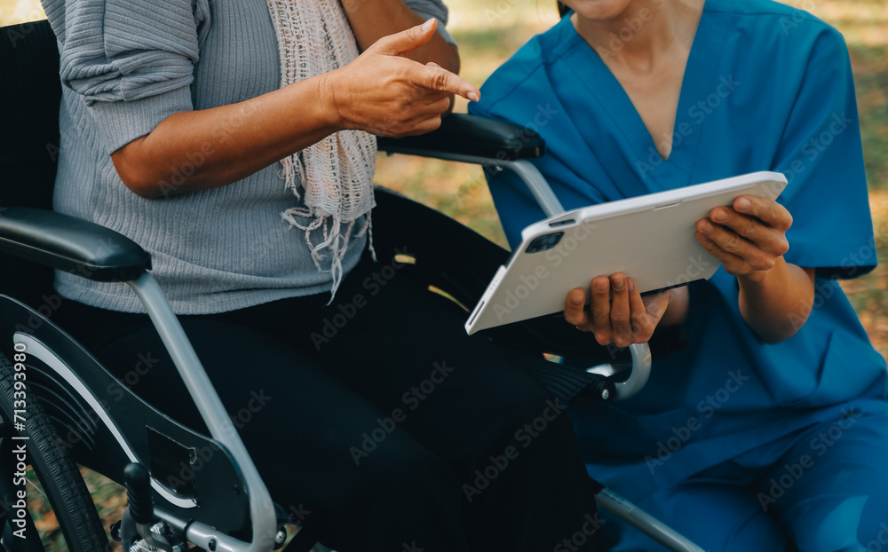 Elderly asian senior woman on wheelchair with Asian careful caregiver and encourage patient, walking in garden. with care from a caregiver and senior health insurance in sun light