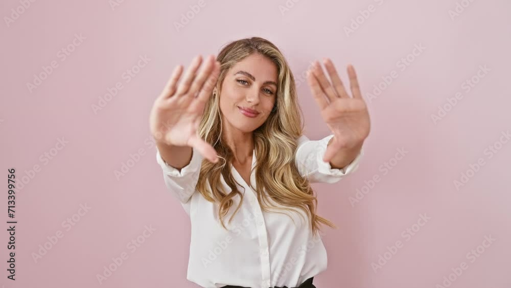 Attractive, young blonde babe in a shirt, creatively making a frame sign with her fingers and palms; a happy, camera perspective shot against a lovely isolated pink background.