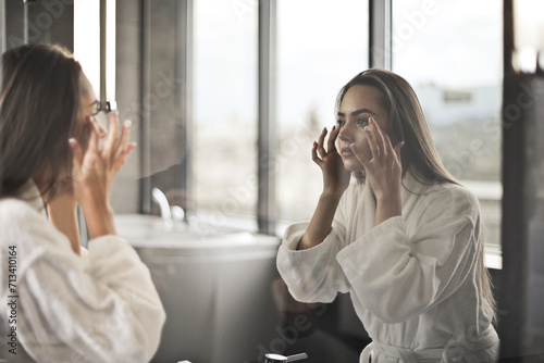 young woman in bathrobe looks at herself in the mirror in the bathroom