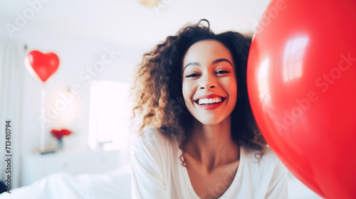 Happy young black woman holding balloon with a red heart and posing for the camera, symbol of love for Valentine's Day