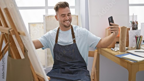 Smiling young man taking selfie indoors, wearing overalls, artist studio background, casual, creative, technology, denim, happiness, education photo
