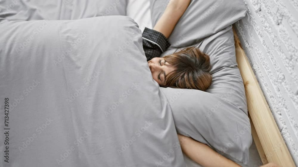 Beautiful young hispanic woman stretching her arms, waking up on a cozy bed in a homey bedroom, looking confident and enjoying the morning comfort.