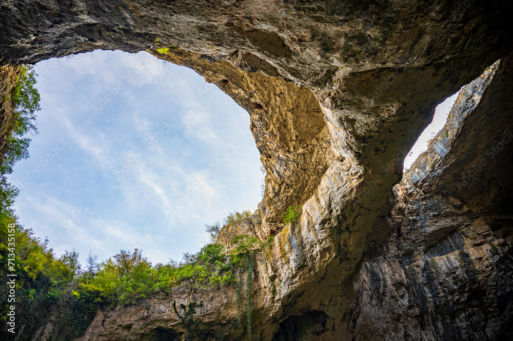 Giant cave with big holes in the sealing, all full of trees and water - Devetashka cave