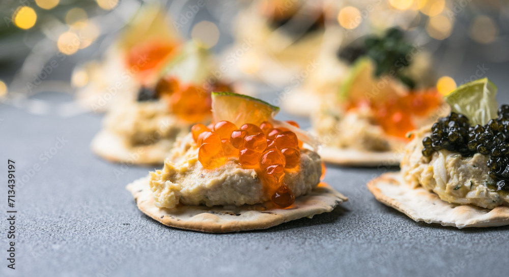 Holiday canapes with red and black caviar, on crackers festive silver Christmas decoration, copy space, selected focus, narrow depth of field
