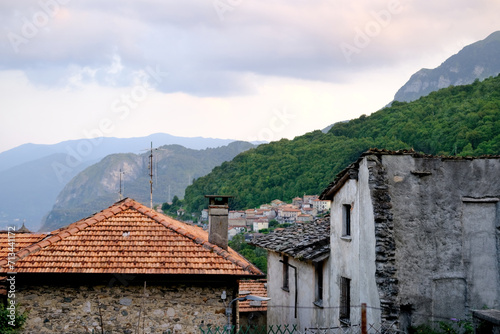 Tile roofs of old buildings, medieval semi-ruined facades against backdrop of mountains, historical architecture of Mediterranean cities #713441172