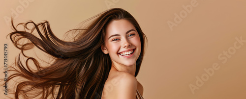 Smiling young pretty woman with brunette brown long groomed hair isolated on pastel flat beige background with copy space. Perfect hair care products banner template, hair salon. photo