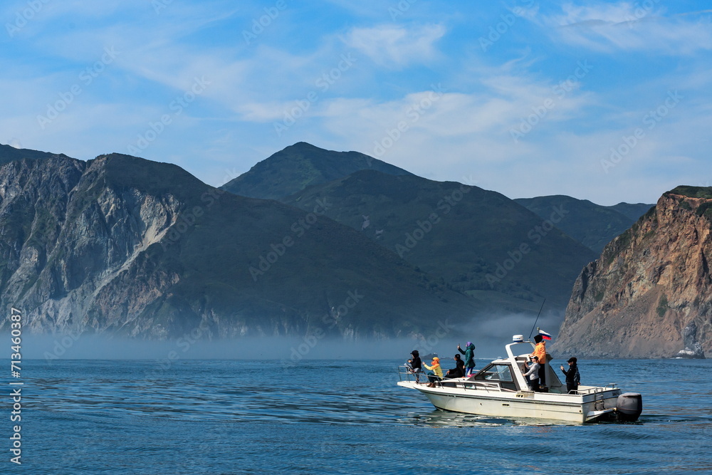 Fishermen sail on a boat against the backdrop of large mountains on the Pacific Ocean, clear sunny day, Kamchatka.