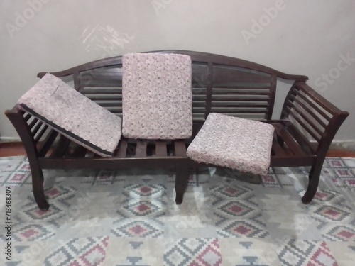 Messed wooden sofa with unorganised cushions in the room with scratch wall background. photo