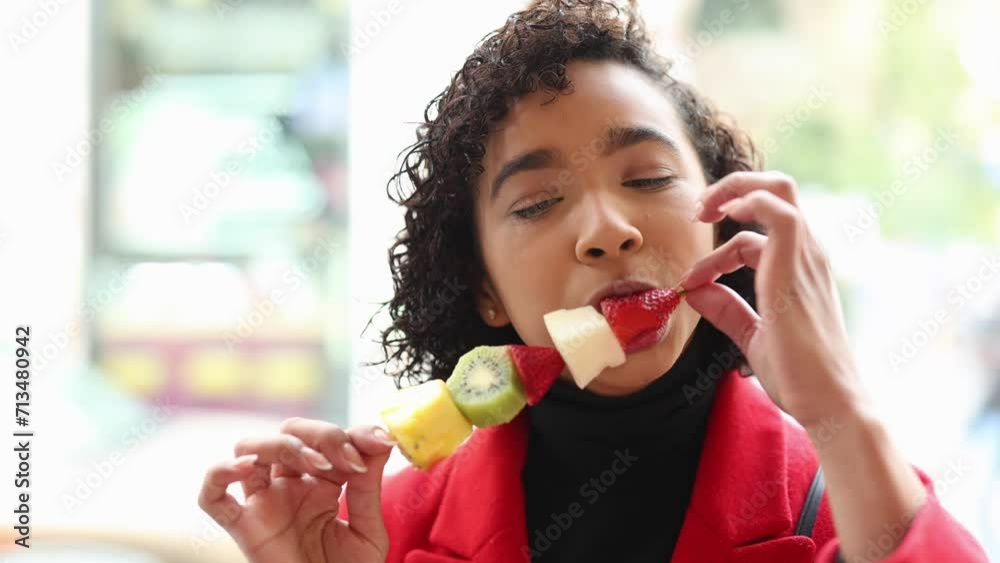 close up portrait of young adult woman eating fruit in front of a window