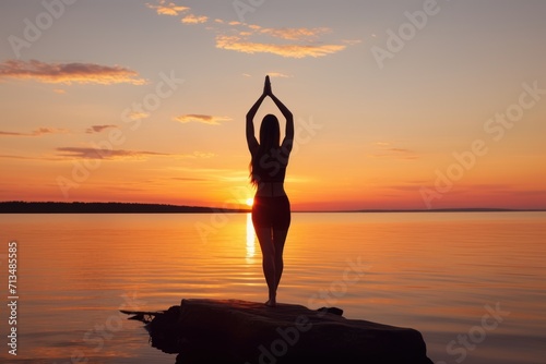  a woman standing on a rock in the middle of a body of water with the sun setting in the background. © Nadia