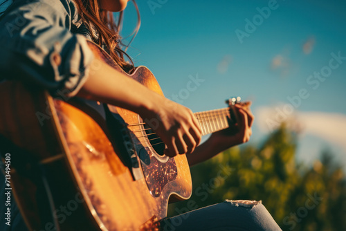 In sunlight, a young artist plays an acoustic guitar in a park, creating melodic beauty. photo