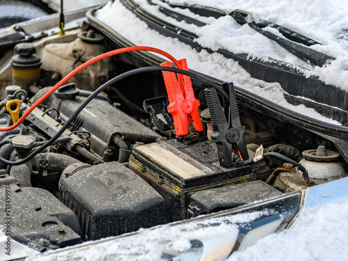 Charging automobile discharged battery by booster jumper cables at winter. Close-up. Problem starting a car in extreme freezing conditions.