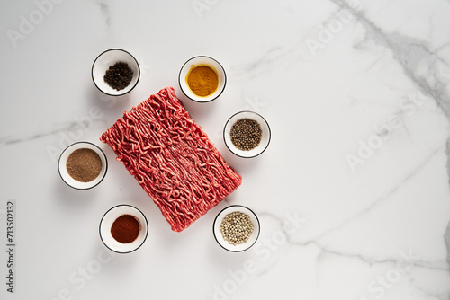 Raw and Fresh Minced Beef on white marble background with spices for cooking. Minimalistic food photo, high-key. Top view, copy space