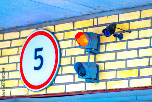 A traffic light with a monitoring camera on the garage wall above the garage door. Traffic signals regulate the entrance to a parking lot, underground parking lot or warehouse. photo