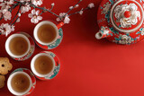 juego de te chino de porcelana compuesto de tetera y tazas de color rojo y decoradas con flores rosas de cerezo, sobre superficie roja. concepto año nuevo chino