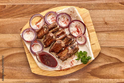 Fried lamb ribs meat with red onion rings, sauce and pita bread on the wooden board on the wooden table, flat lay top view