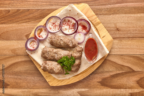 Fried meat kebabs with red onion rings, sauce and pita bread on the wooden board on the wooden table, flat lay top view