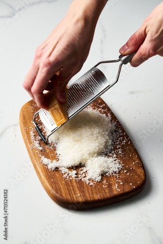 Man hands grating parmesan cheese on a wooden board. White, bright and clean background.