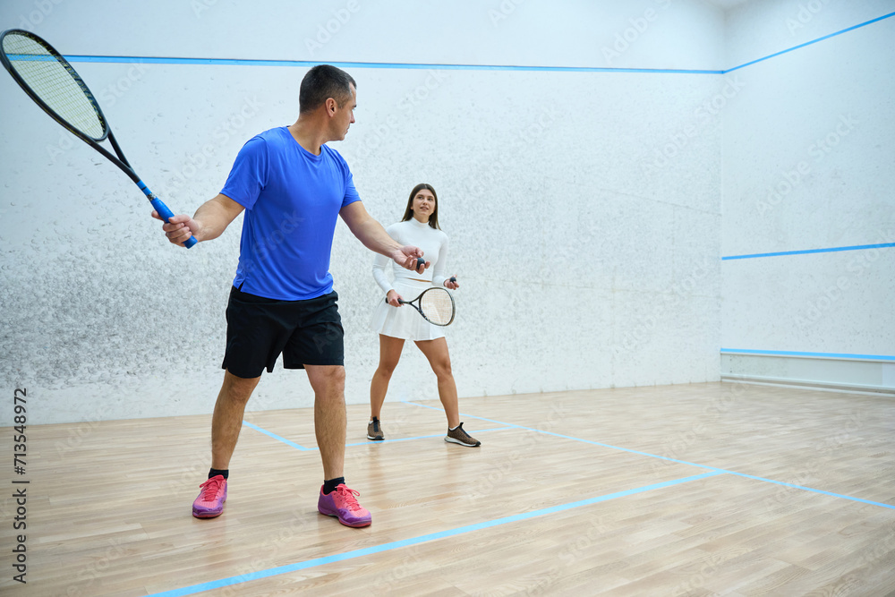 Man instructor fervently teaching woman to play squash exercising