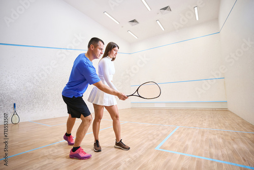 Man instructor guides woman emphasizing precise squash hitting techniques