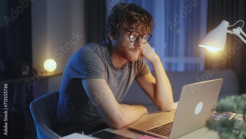 Boring tired red haired man student or freelancer with study or work at home workplace at late night Stressed male exhausted from remote distance work or education and hard program indoors photo