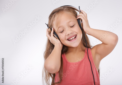 Girl kid, music and happy with headphones in studio for audio, subscription and streaming multimedia on white background. Child, smile and listening to podcast, hearing sound and radio connection
