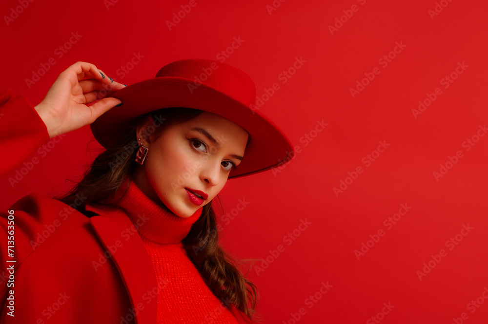 Fashionable confident woman wearing trendy red hat, knitted turtleneck sweater, coat, silver earrings, posing on red background. Close up studio fashion portrait. Copy, empty space for text Fashionable confident woman wearing trendy red hat, knitted turtleneck sweater, coat, silver earrings, posing on red background. Close up studio fashion portrait. Copy, empty space for text