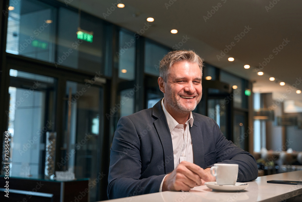 Fototapeta premium Adult smiling man drinking tea or coffee from cup and looking at camera