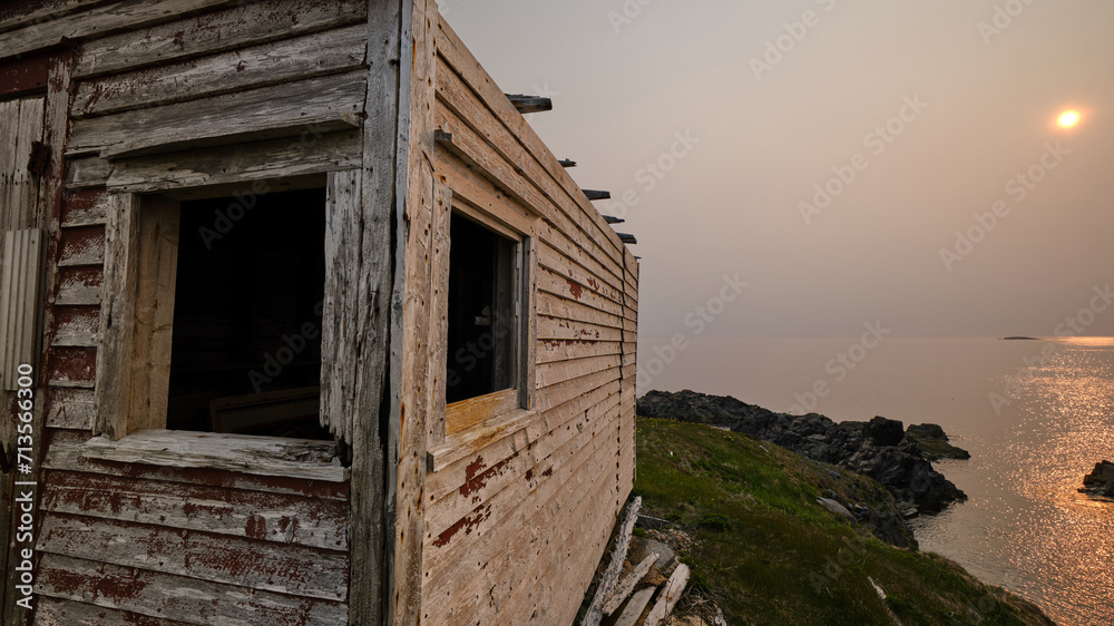 Abondoned weathered wooden fishing shacks on the windswpt and desolate coast of Newfoundland with the sun going down