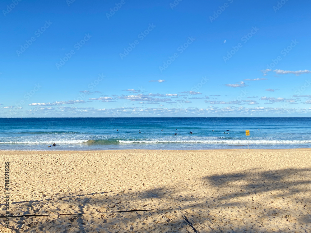 Surfers practicing catching a wave in the turquoise-blue ocean. Surf lesson. A day at the beach on a sunny day. Beach shore with sky and clouds. Surfers practicing catching a wave in the turquoise-blue ocean. Surf lesson. A day at the beach on a sunny day. Beach shore with sky and clouds.