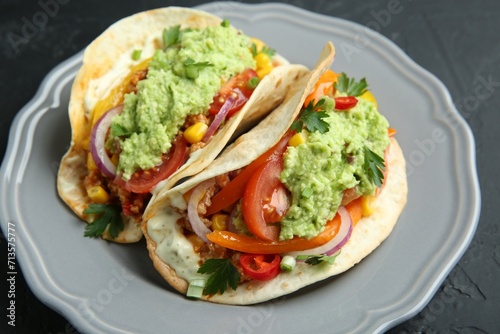Delicious tacos with guacamole, meat and vegetables on black table, closeup