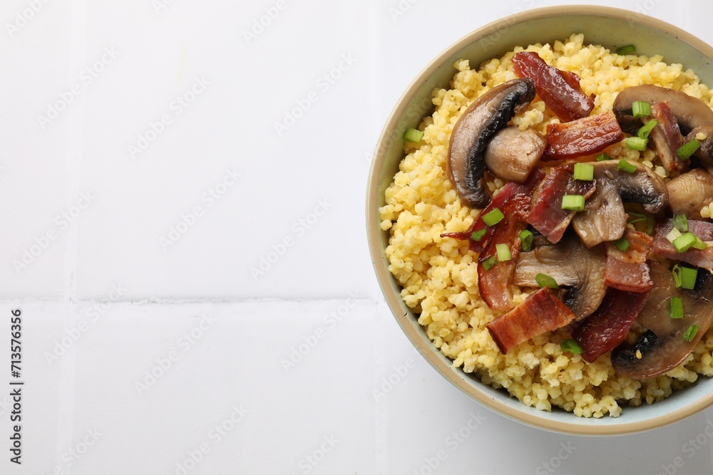 Tasty millet porridge with mushrooms, bacon and green onion in bowl on white tiled table, top view. Space for text Tasty millet porridge with mushrooms, bacon and green onion in bowl on white tiled table, top view. Space for text