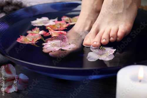 Woman soaking her feet in bowl with water and flowers on wooden floor, closeup. Spa treatment