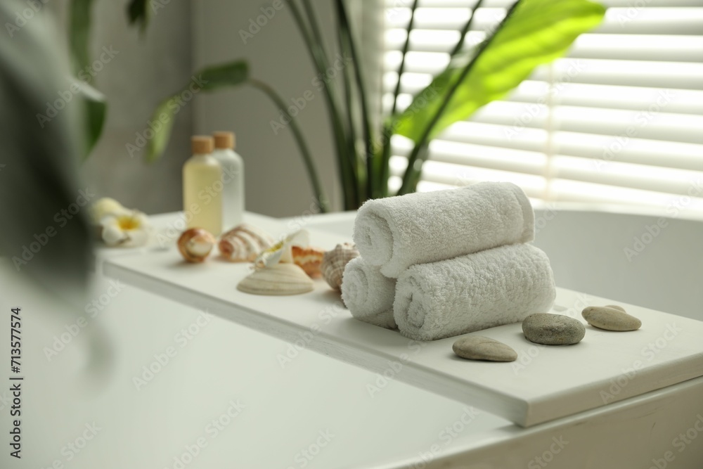Bath tray with spa products and towels on tub in bathroom