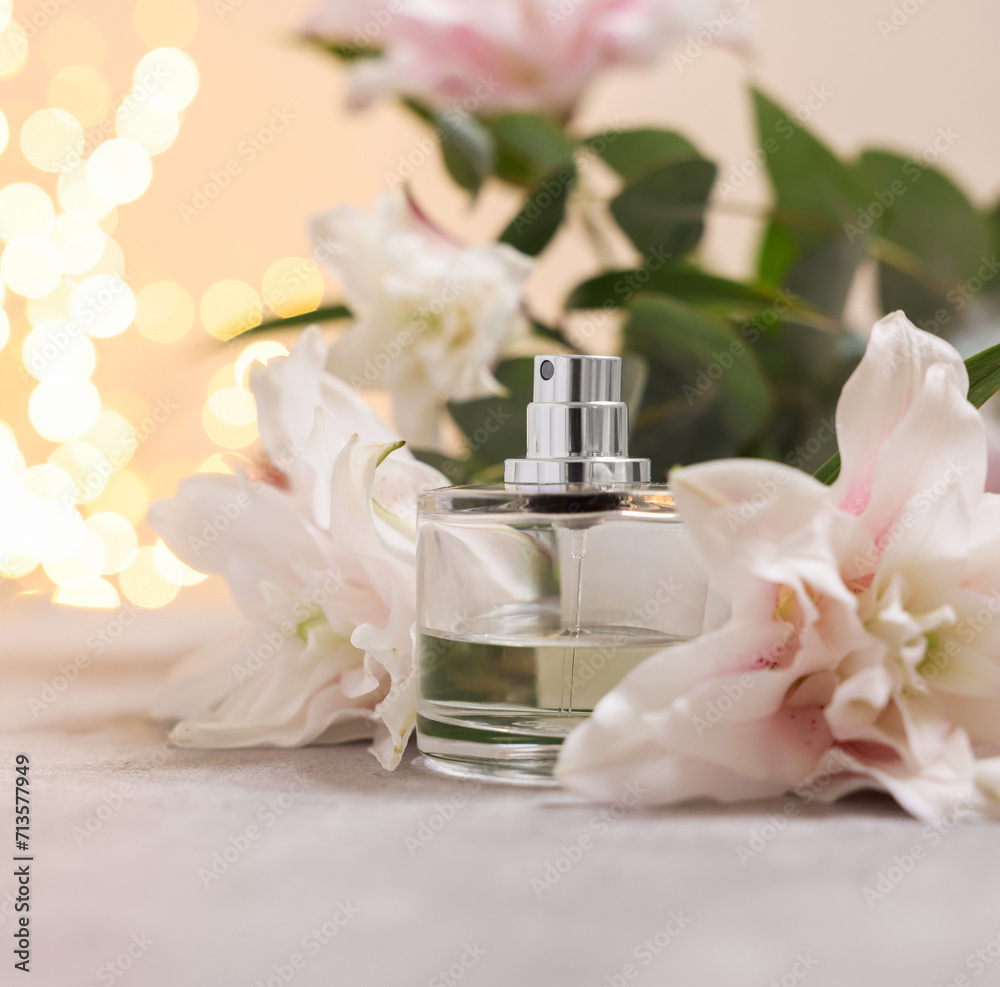 Bottle of perfume and beautiful lily flowers on table against beige background with blurred lights, closeup Bottle of perfume and beautiful lily flowers on table against beige background with blurred lights, closeup