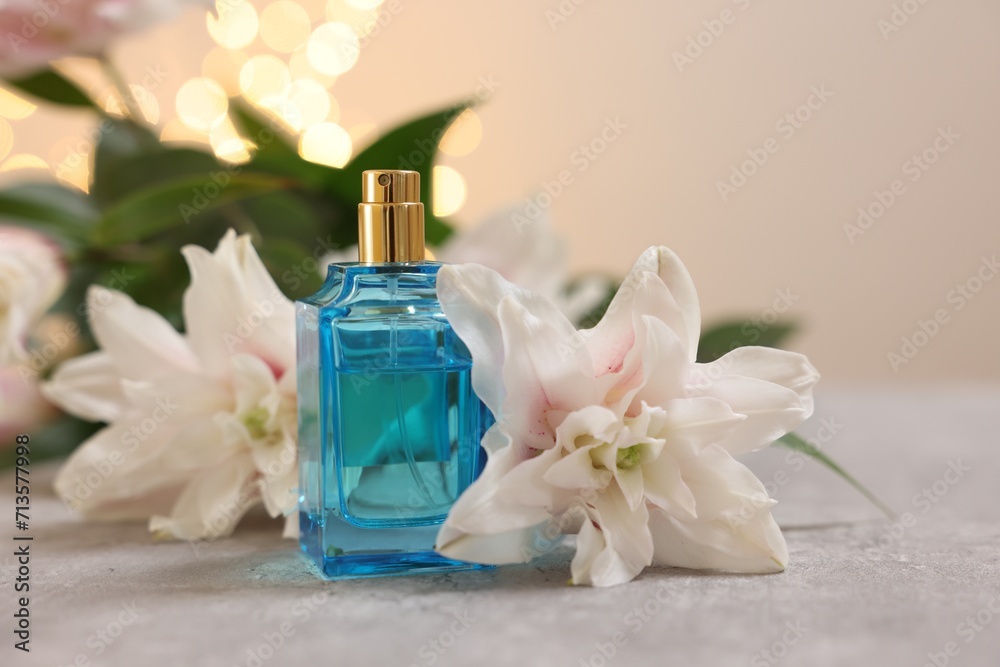 Bottle of perfume and beautiful lily flowers on table against beige background with blurred lights, closeup Bottle of perfume and beautiful lily flowers on table against beige background with blurred lights, closeup