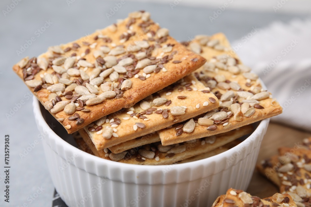 Cereal crackers with flax, sunflower and sesame seeds in bowl on grey table, closeup