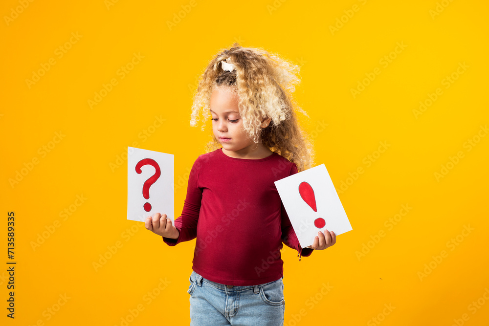 Fototapeta premium Enchanting Exploration. A Portrait of a Thoughtful child Girl Holding Cards with Question Marks and Exclamation Points.
