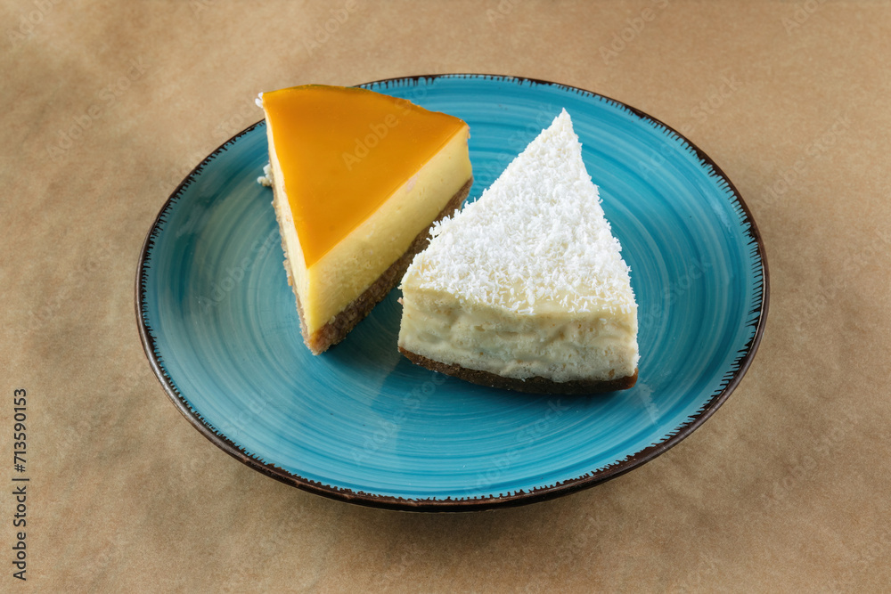 A slice of coconut cheesecake and a slice of orange cheesecake on a blue plate.